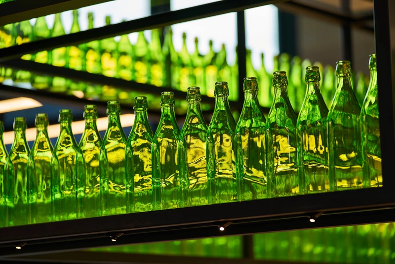 Backlit green glass bottles on black metal bar shelving