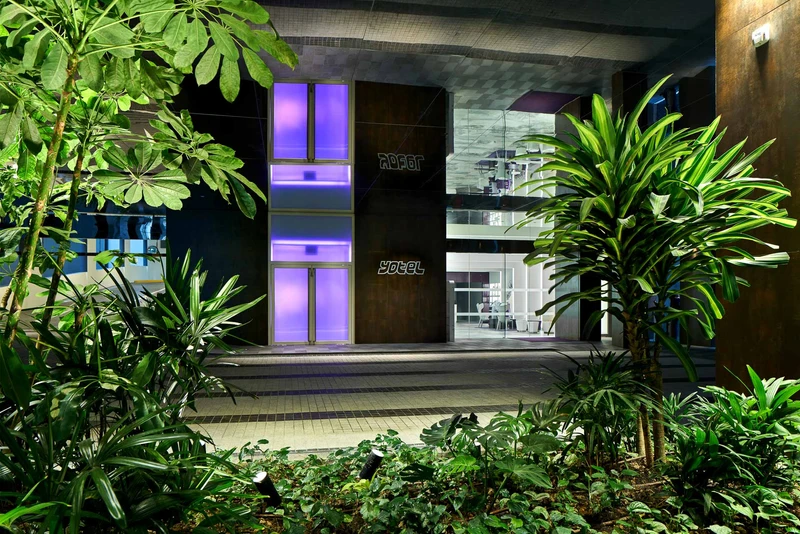 Corten steel facade with purple glass panels and tropical landscaping at night