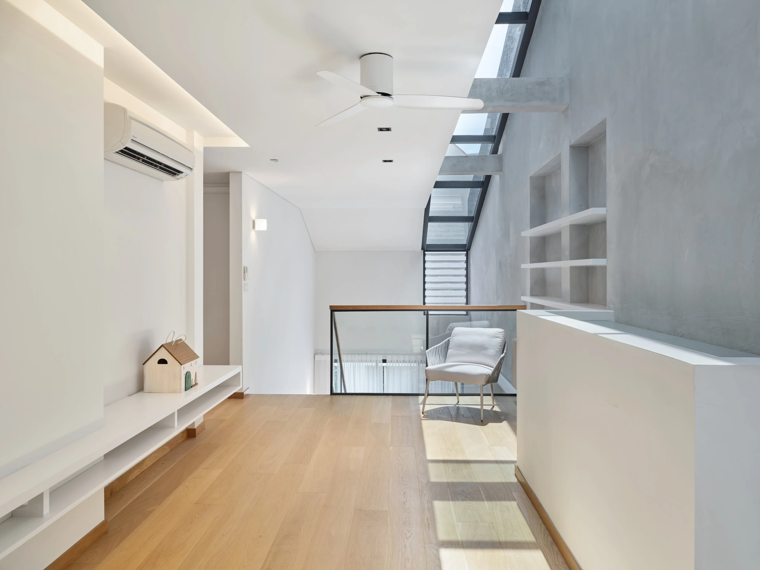 Upper-floor landing with oak flooring, concrete feature wall, skylight strip, white ceiling fan, and built-in shelving