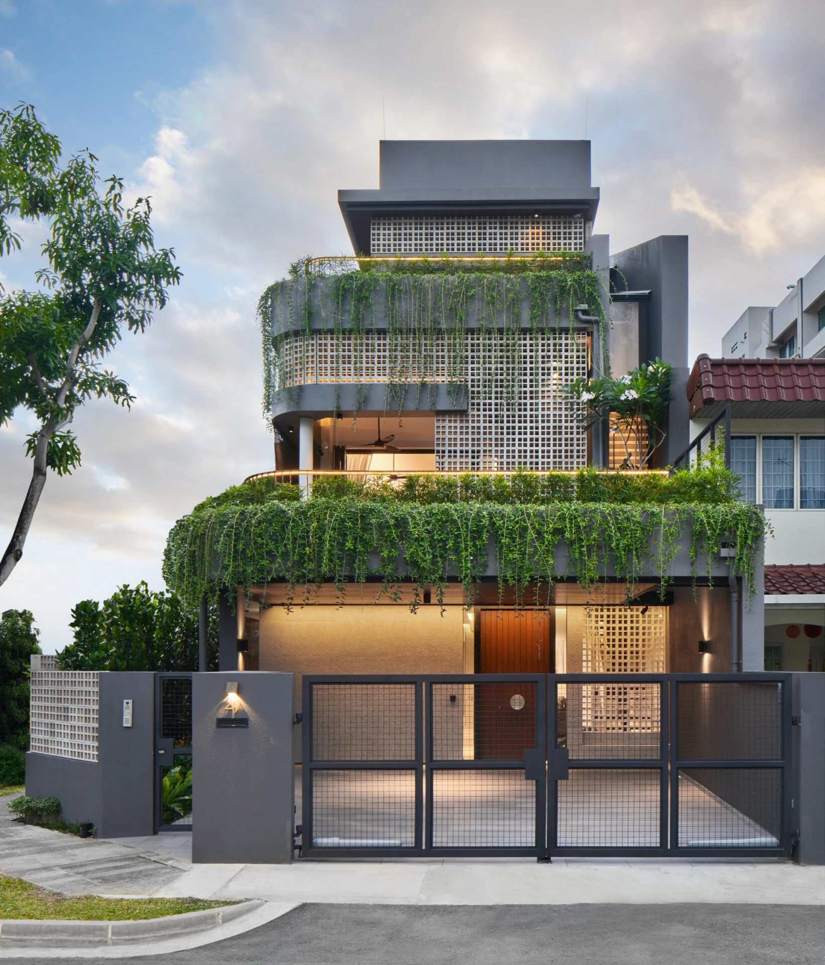 Front facade of modern tropical home with perforated screens, trailing plants on each level, and metal entry gate