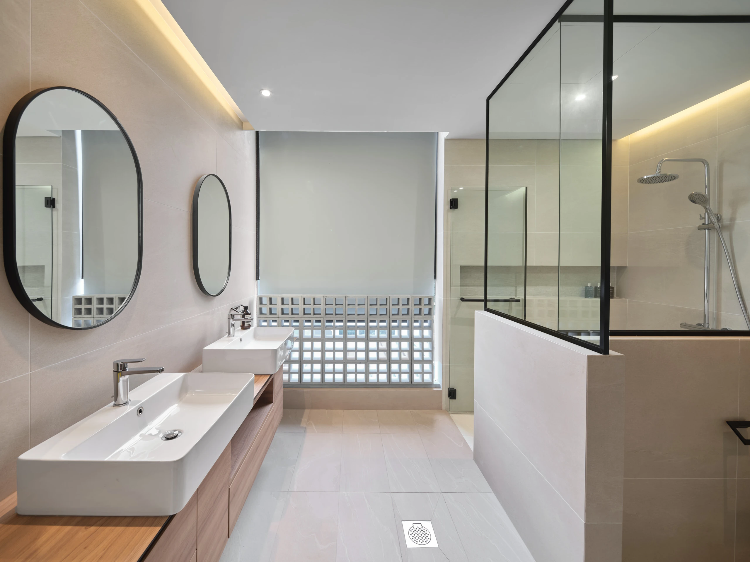 Bright bathroom with dual vessel sinks, oval mirrors, breeze-block window wall, and black-framed glass shower enclosure
