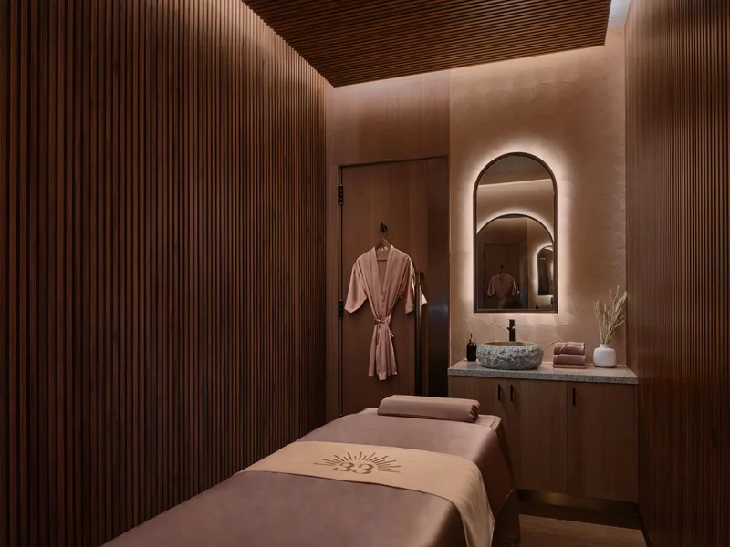 Warm spa treatment room with slatted wood walls, massage bed and arched mirror