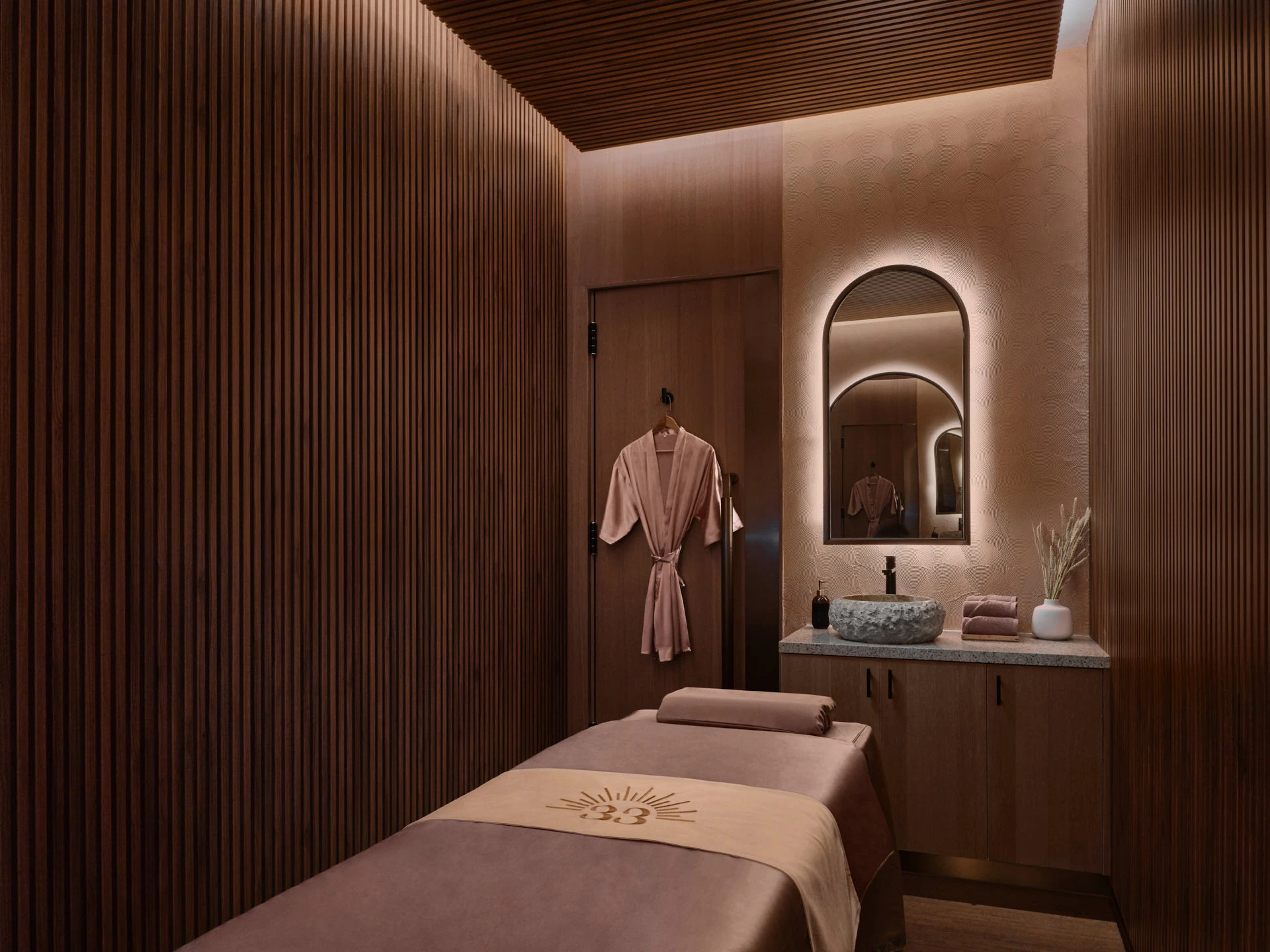 Spa treatment room with timber slat walls, stone basin and branded table