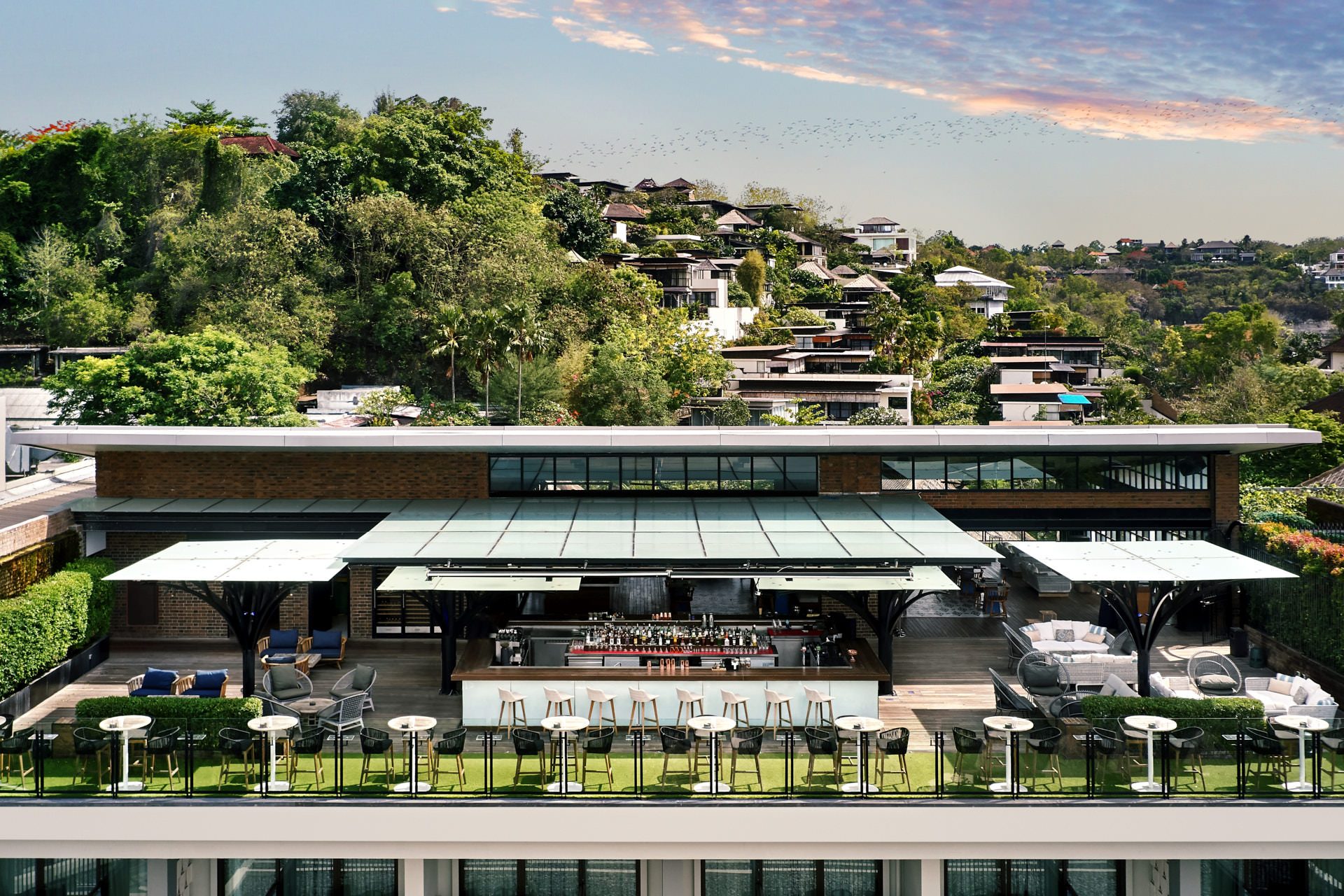 Rooftop bar at golden hour with steel canopy columns and Balinese hillside views