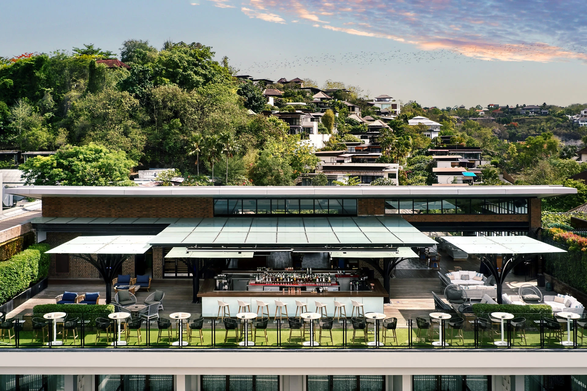 Rooftop bar at golden hour with steel canopy columns and Balinese hillside views
