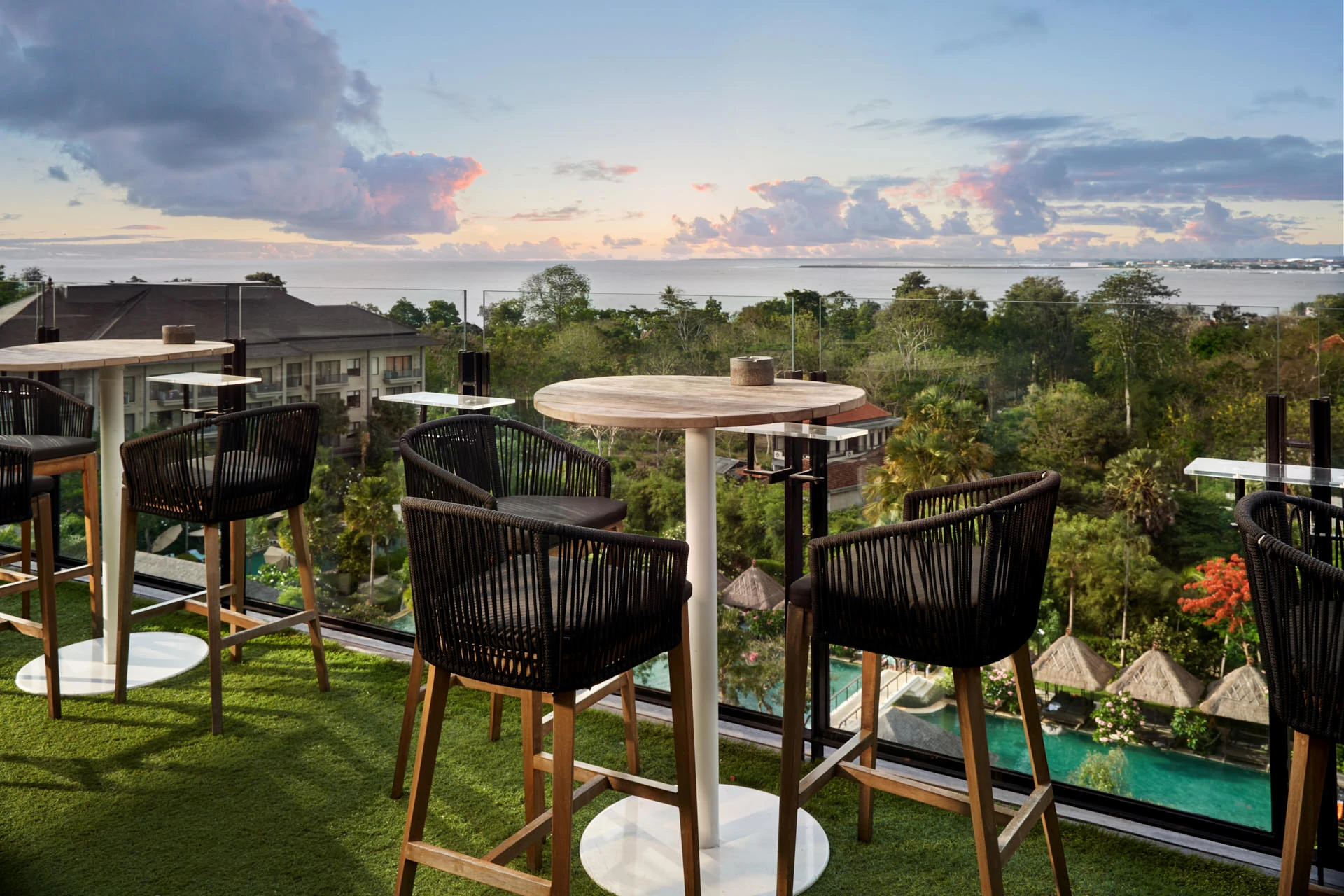 Rooftop bar stools on turf overlooking pool and tropical canopy at sunset