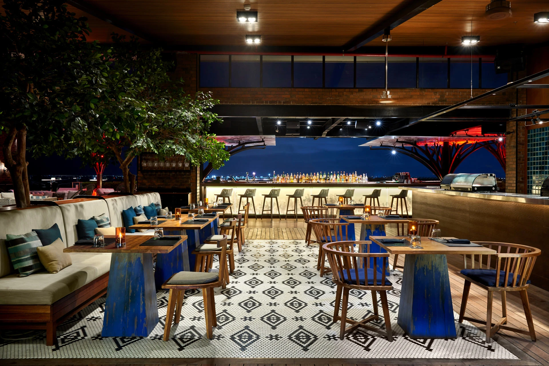 Dining room with mosaic floor, trestle tables and indoor tree at night