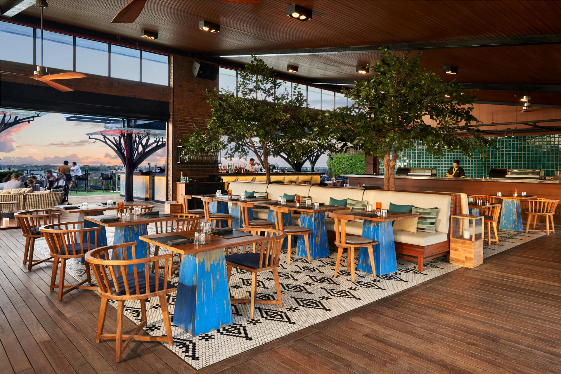 Restaurant at dusk with open kitchen, indoor trees and sunset through canopies