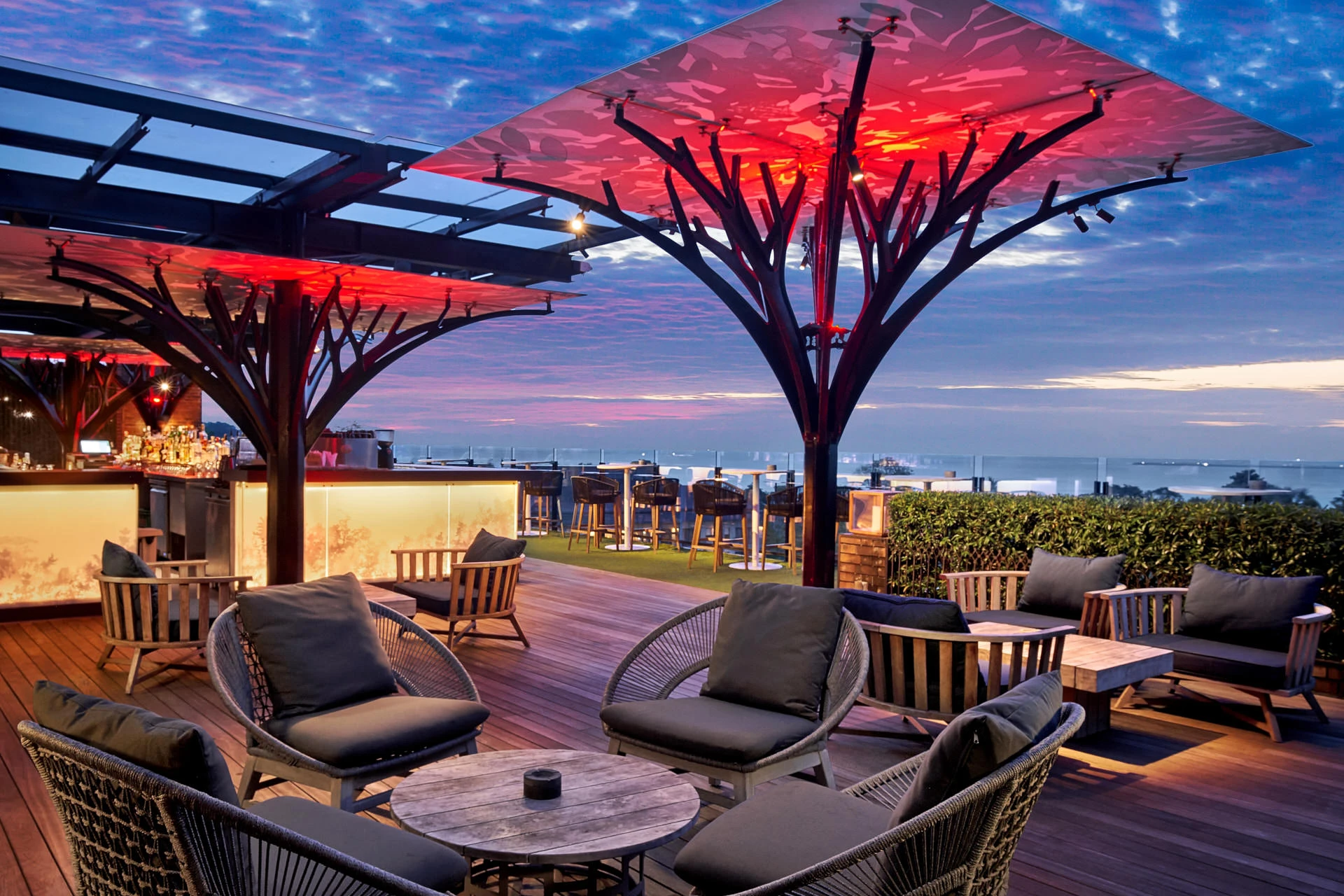 Twilight terrace with rope chairs and red-lit canopy against sunset sky