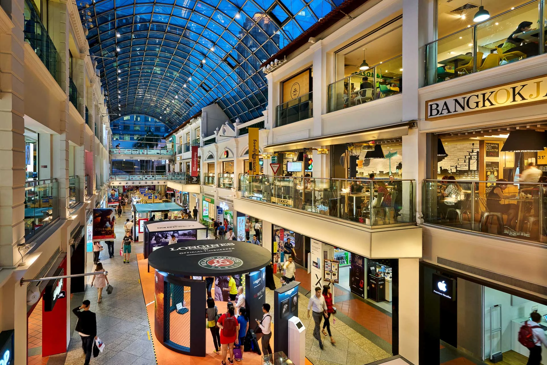 Glass atrium at blue hour with warm retail lighting and shoppers - Bugis Junction Singapore architectural photography
