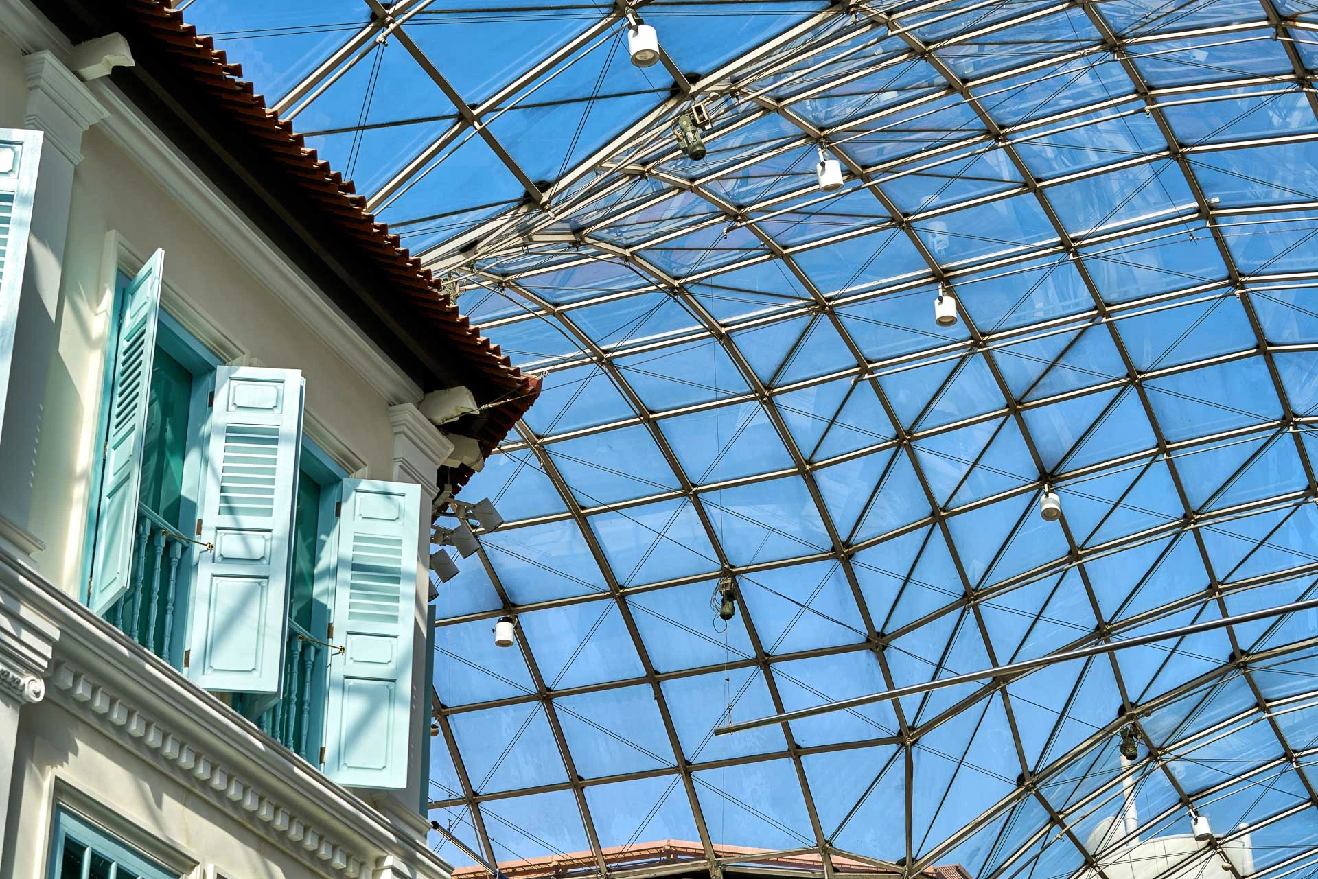 Mint-green shuttered window against geodesic glass canopy and blue sky - Bugis Junction Singapore architectural detail