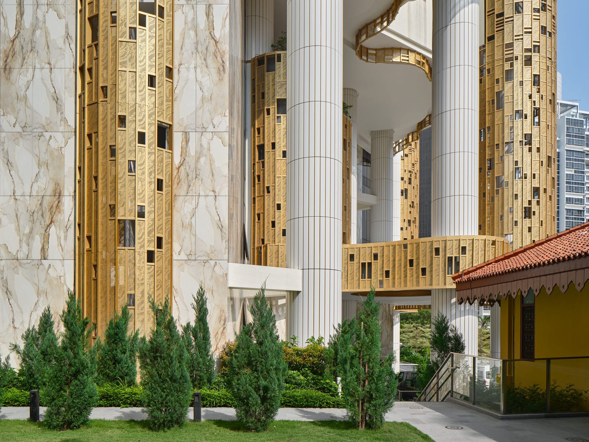 Klimt Cairnhill facade detail with Atlas Concorde gold mosaic tile panels, marble-effect porcelain cladding, and landscaped garden