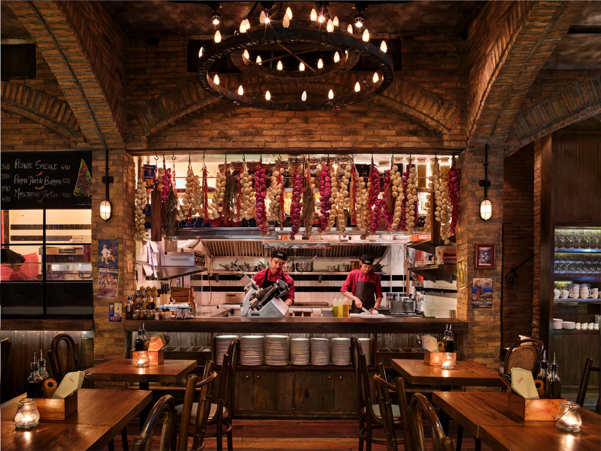 Open kitchen with brick arch, iron chandelier and hanging garlic — Cantina Bangkok restaurant photography