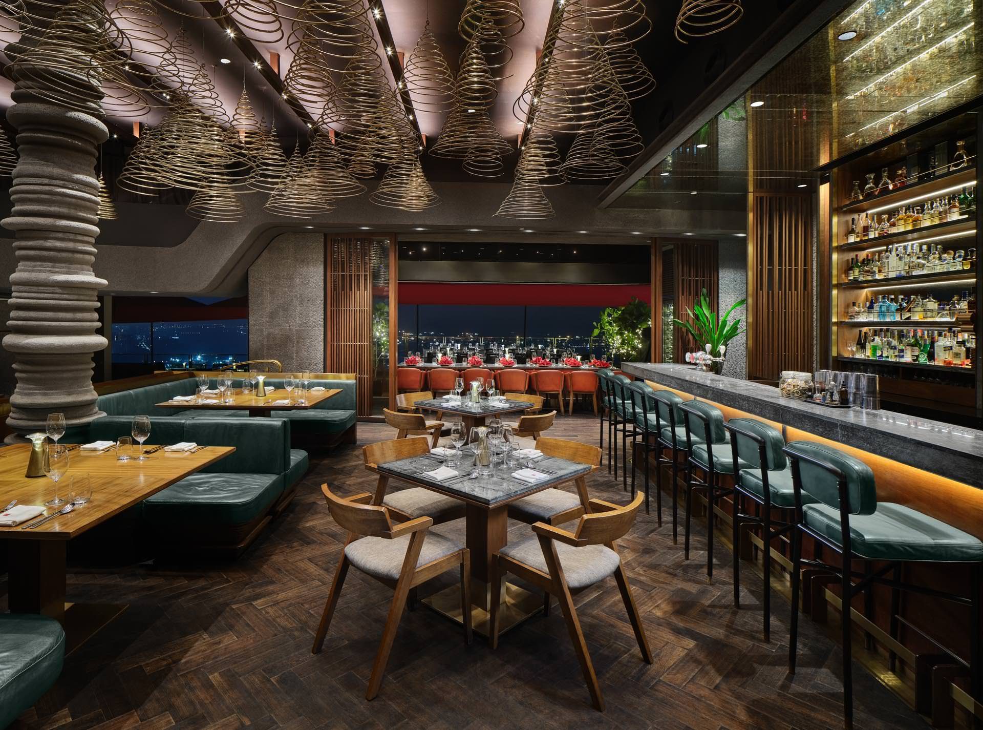 Upper dining level with spiral cone ceiling pendants, herringbone timber floor, teal leather banquettes, mid-century wooden chairs, and a backlit bar with illuminated bottle display at CÉ LA VI Singapore