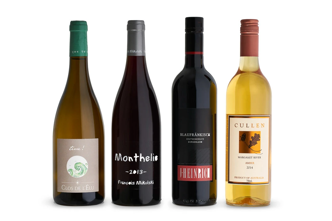 Four wine bottles in a row on a white background: Clos de l’Elu white, Monthelie 2013 red, Blaufrankisch red, and Cullen Amber 2014.