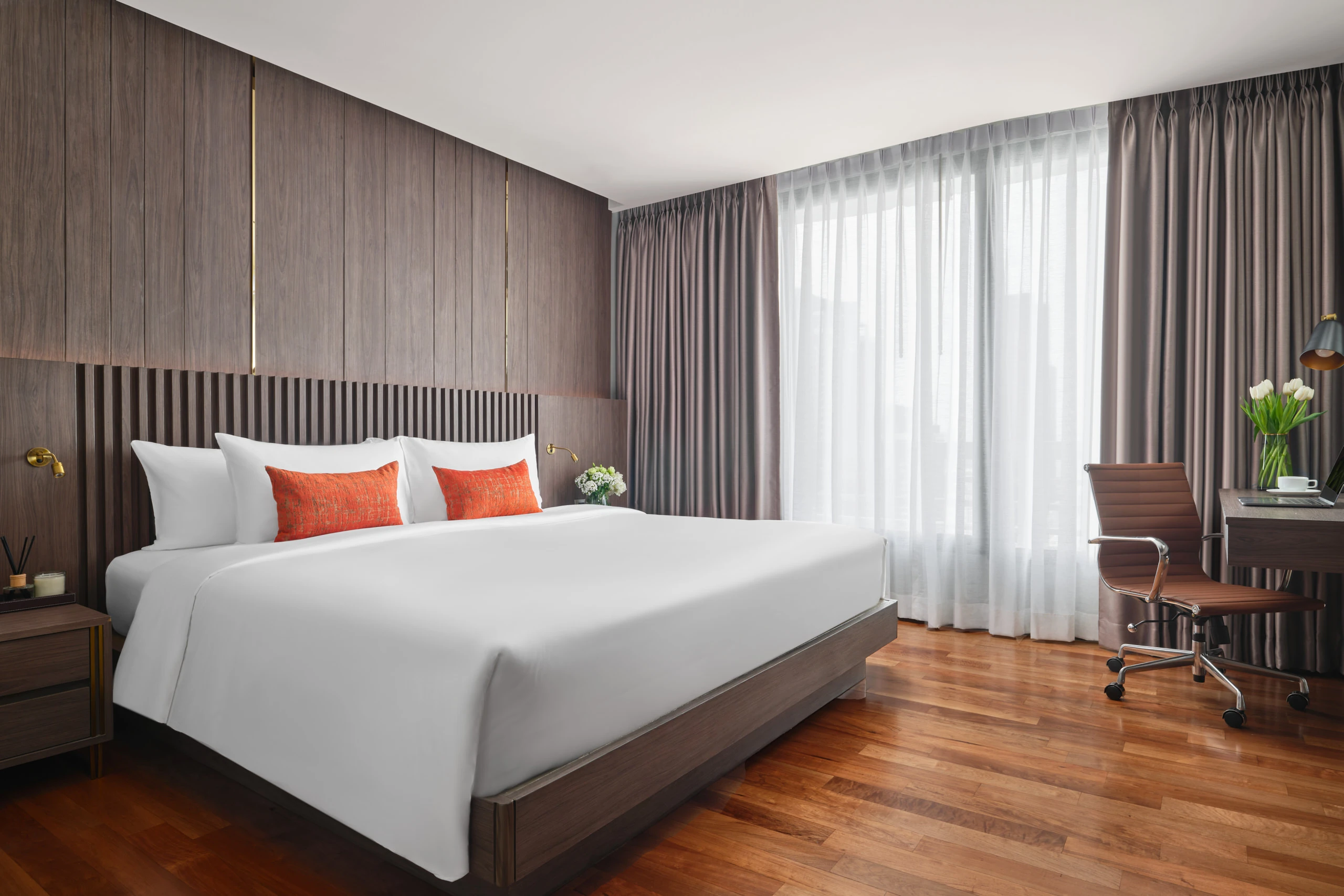 King bedroom with orange pillows, walnut panelling and brass sconces