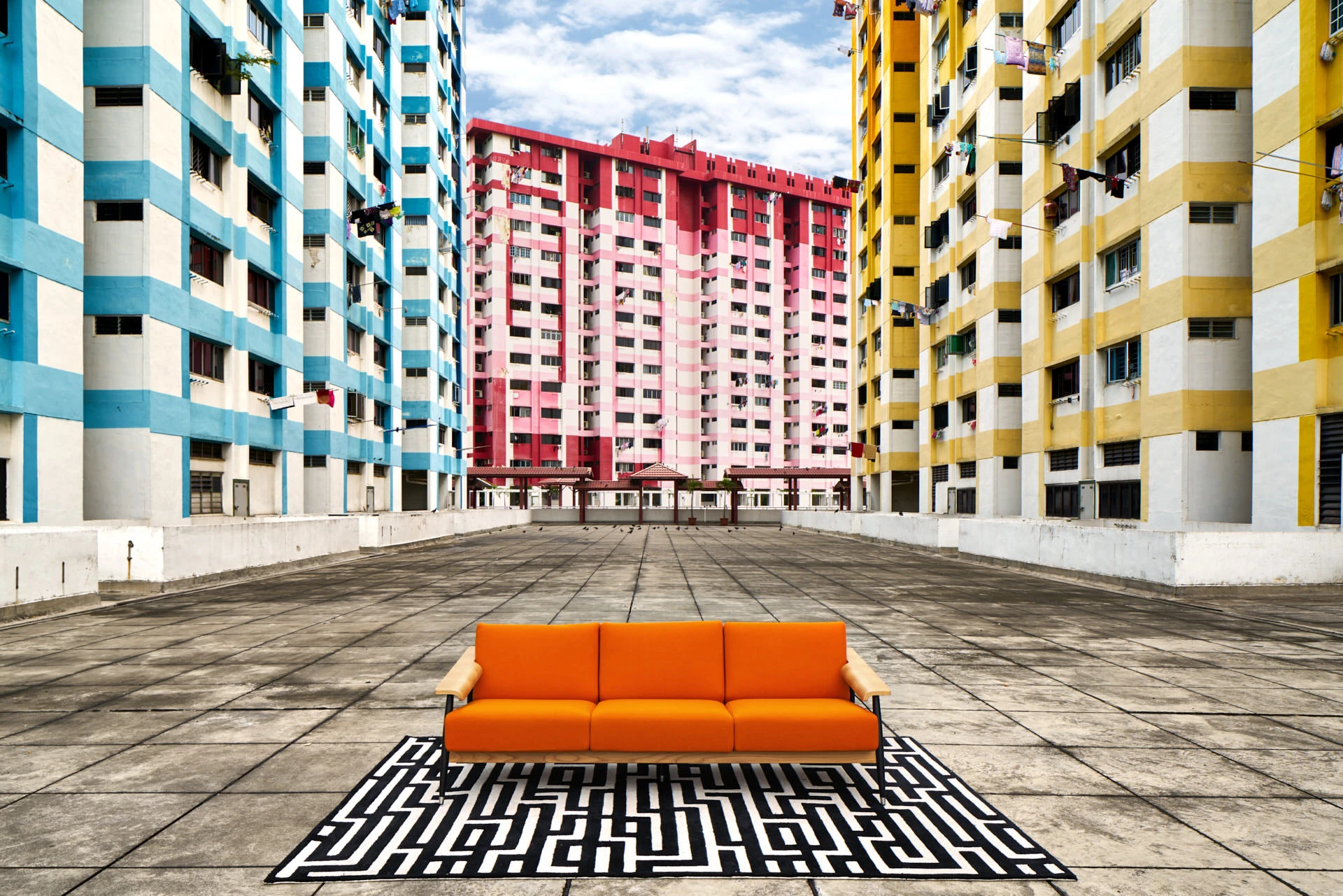 Orange sofa on geometric rug flanked by colourful HDB flats at Rochor Centre
