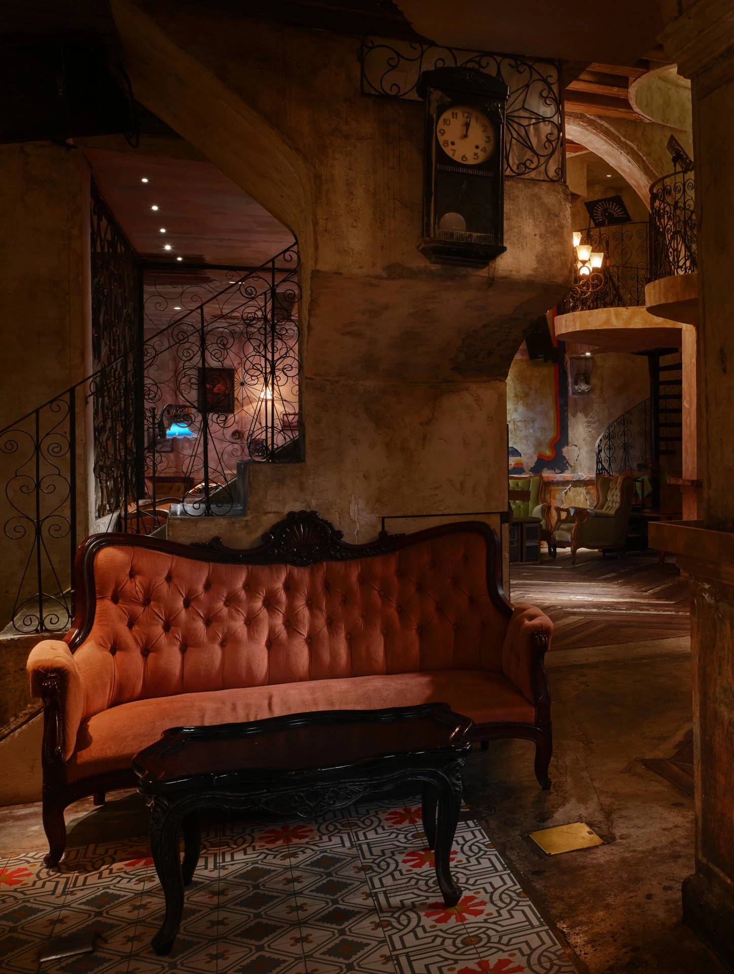 Coral settee beneath antique clock and iron balustrade — Havana Social Bangkok interior photography