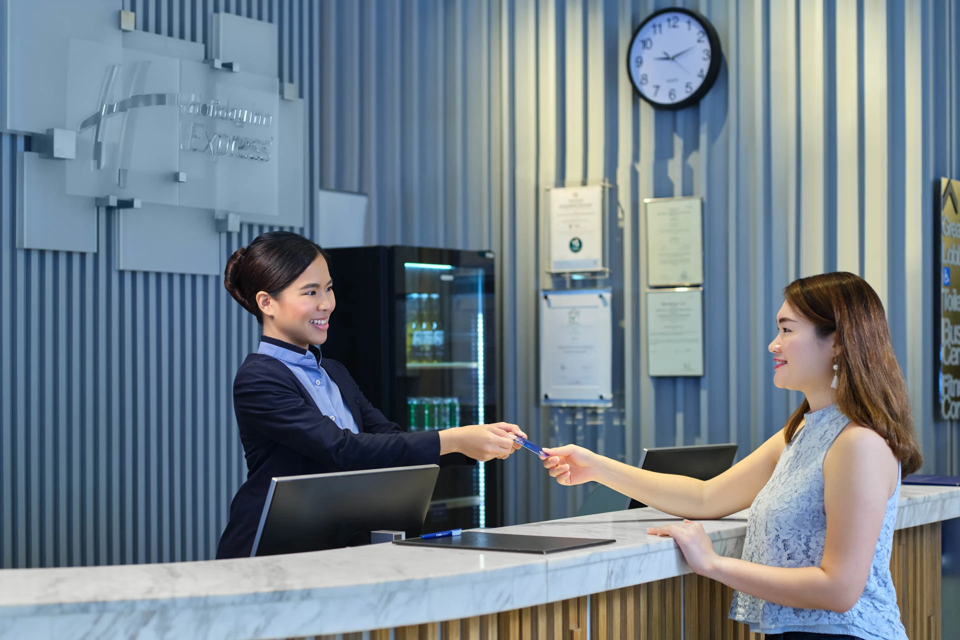 Receptionist handing key card to guest at marble-topped front desk with blue ribbed wall paneling