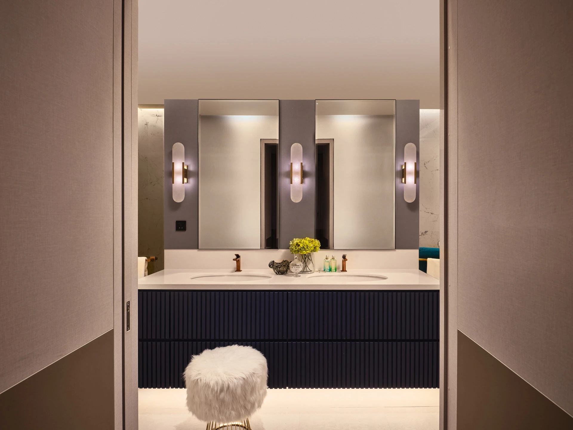 Navy fluted vanity with capsule sconces and faux-fur stool