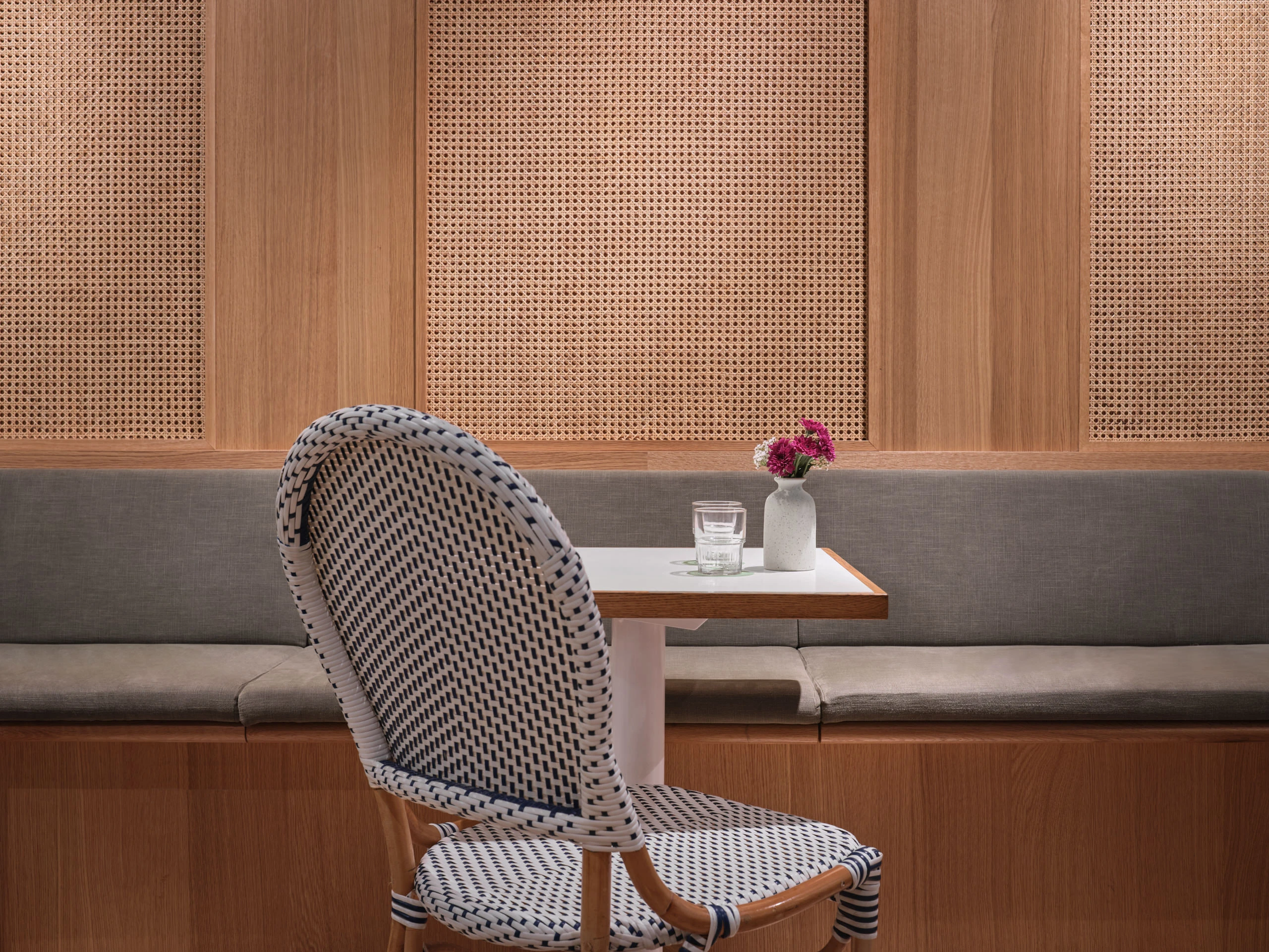 Woven chairs and wooden table detail with greenery backdrop