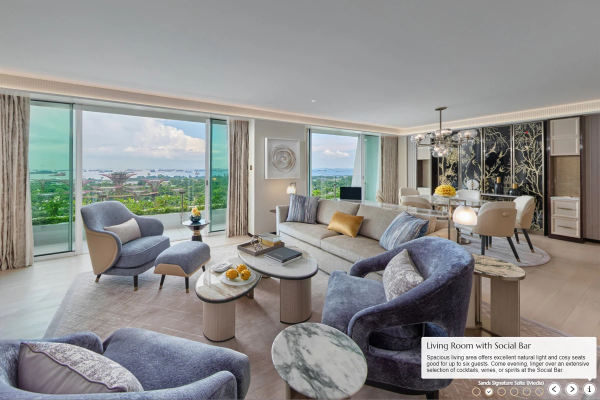 Virtual tour of a luxury hotel suite living room with blue-grey armchairs, beige sofa, marble side tables, floor-to-ceiling windows overlooking gardens and harbor.