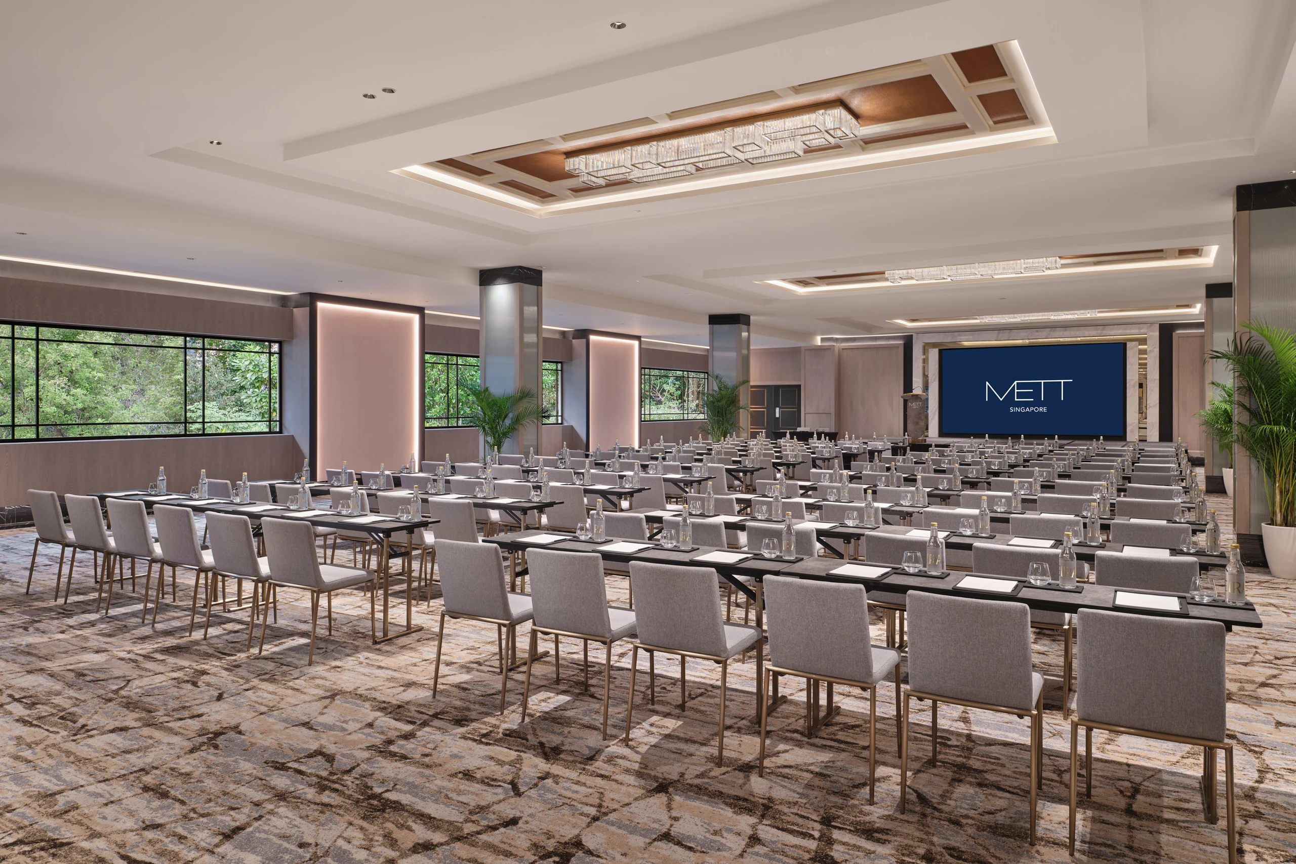 METT Singapore Grand Ballroom set in classroom layout with presentation screen, meeting tables, chandeliers, and Fort Canning Park greenery outside