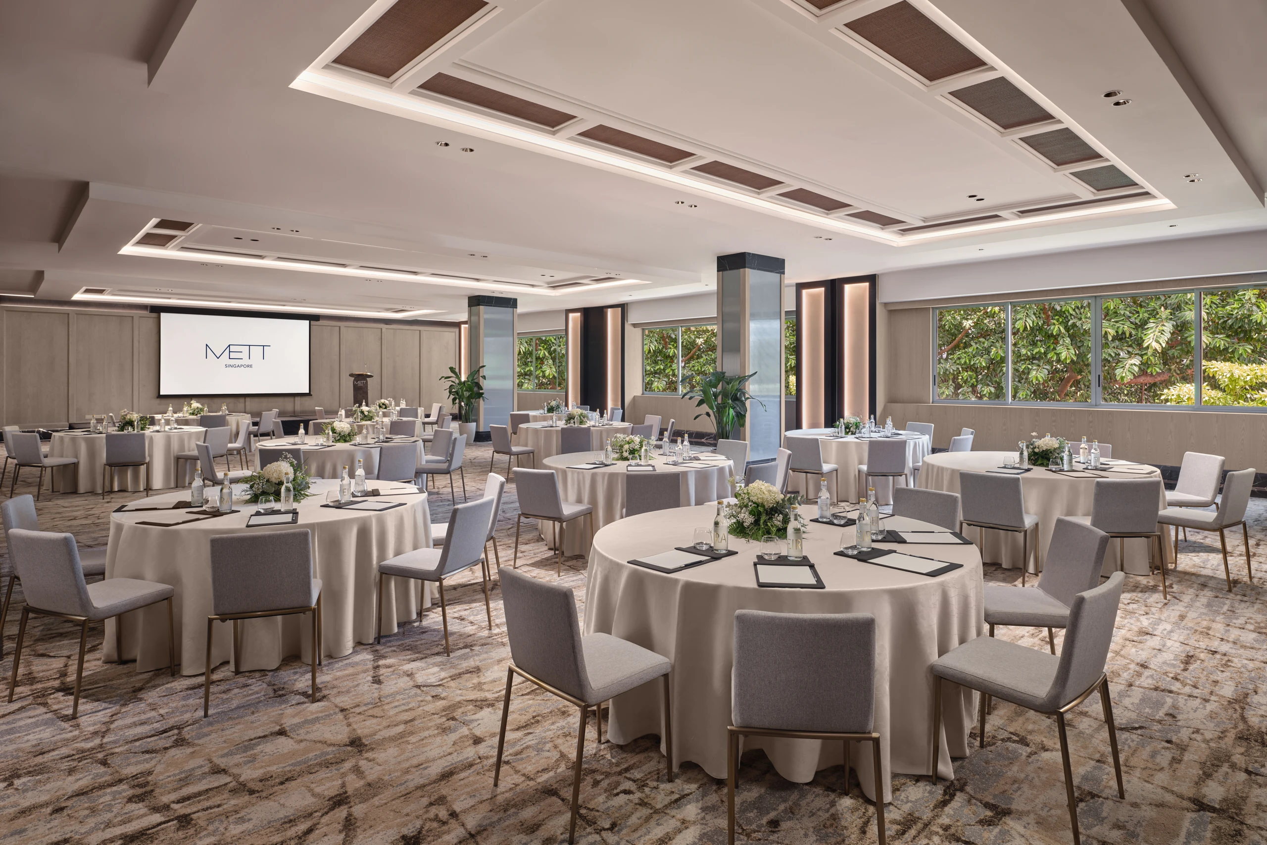 METT Singapore Junior Ballroom cluster setup with round event tables, presentation screen, ceiling panels, and Fort Canning Park greenery