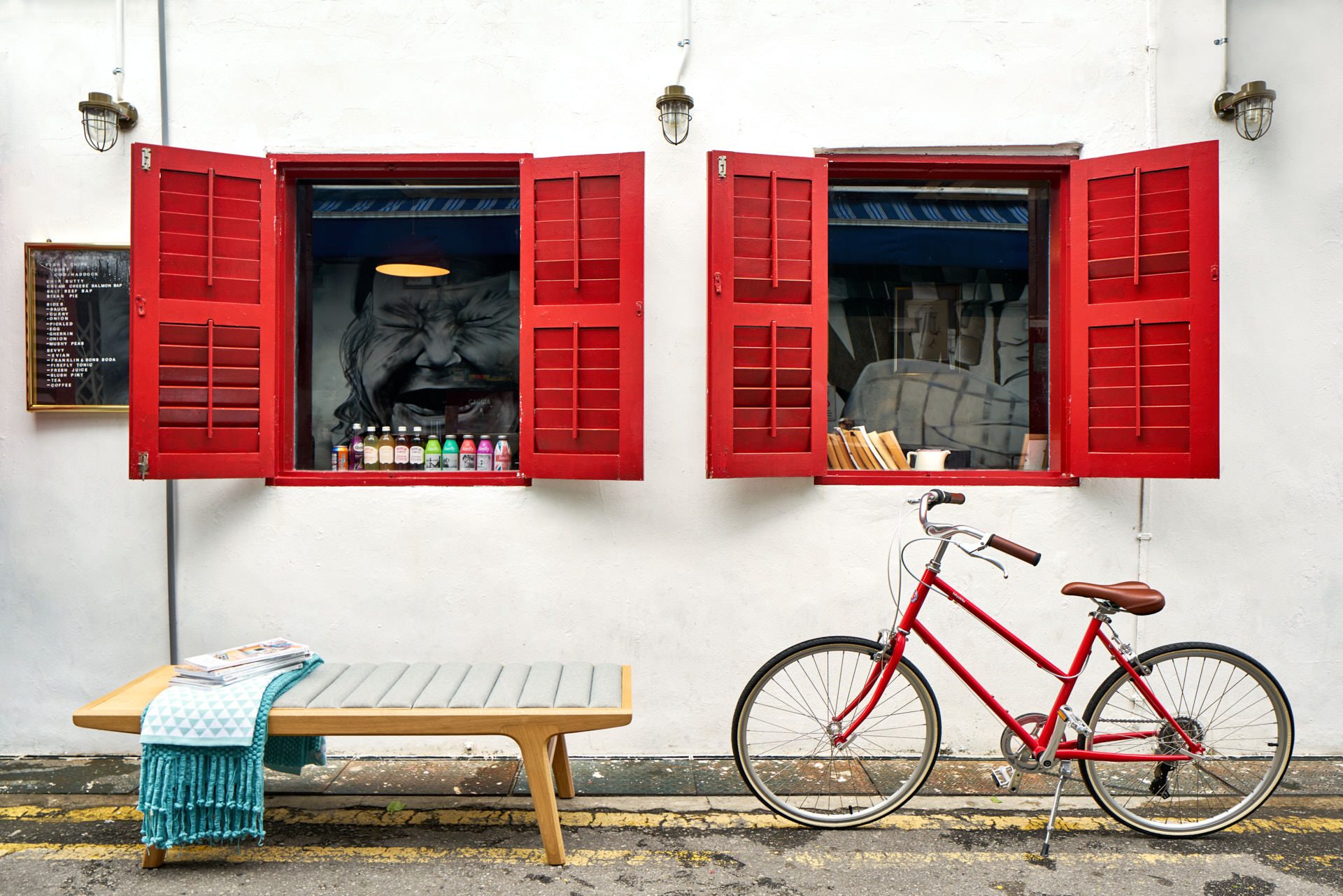 Slatted bench with teal throw beside red vintage bicycle and shuttered windows