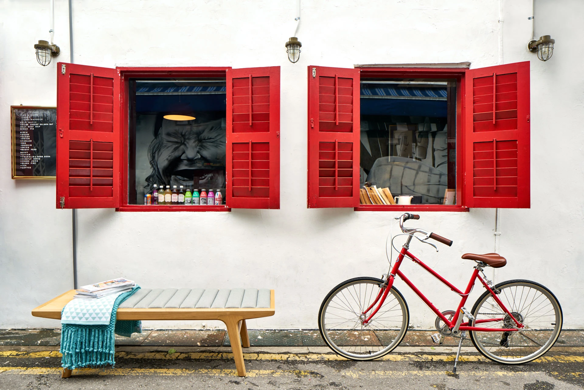 Slatted bench with teal throw beside red vintage bicycle and shuttered windows