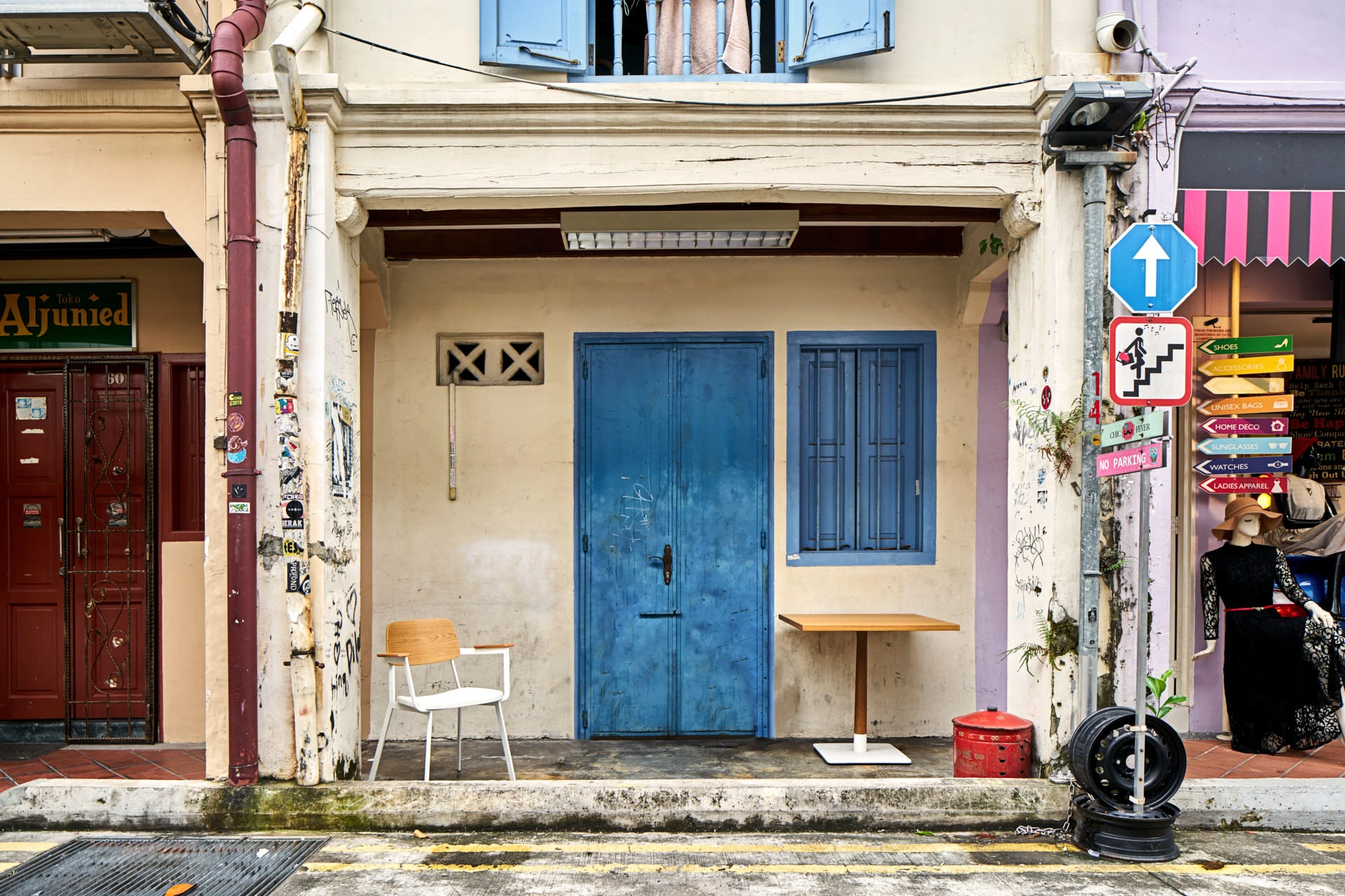 Wooden chair and cafe table beside blue shophouse door and graffiti