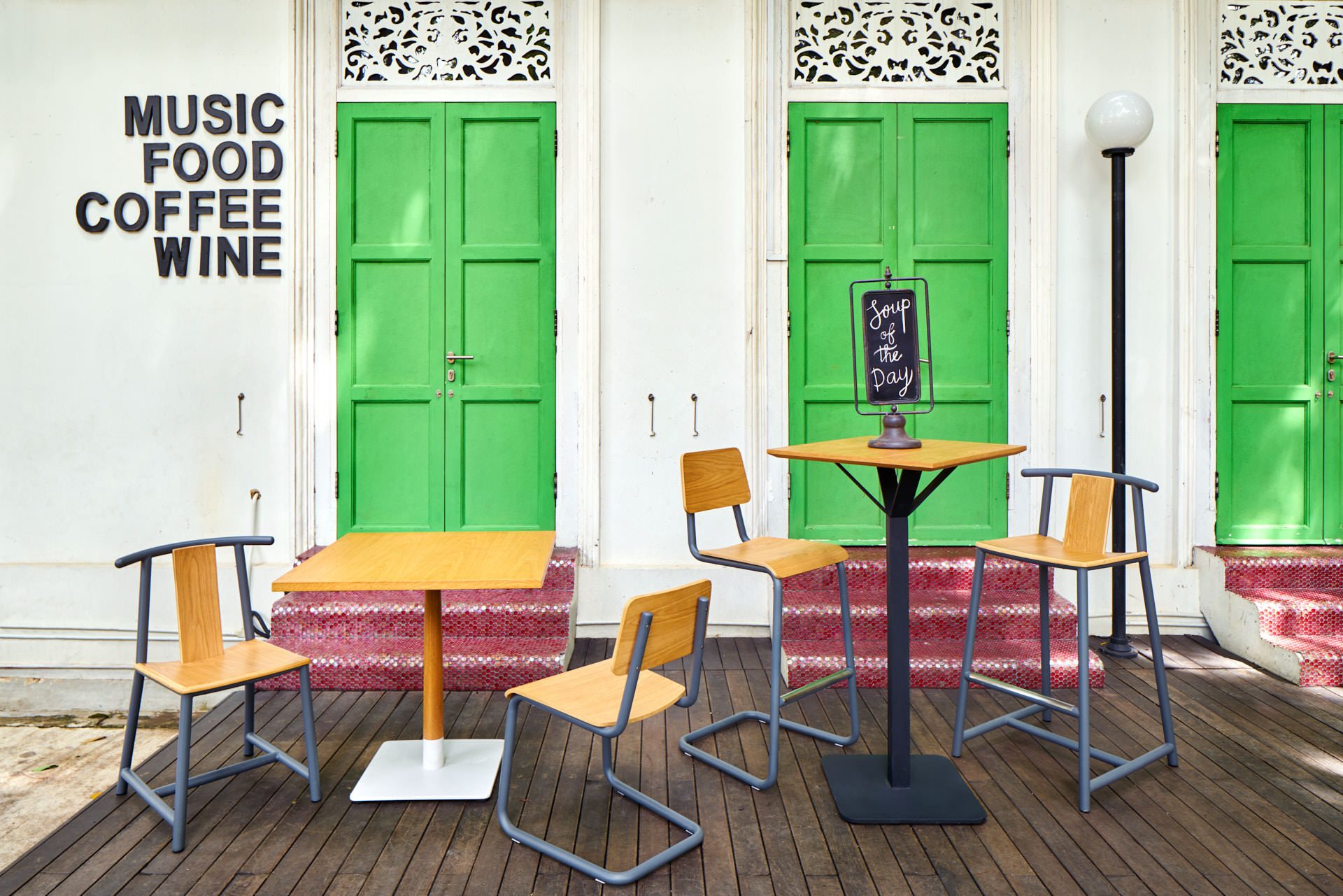 Cafe tables on timber deck before green colonial shophouse doors