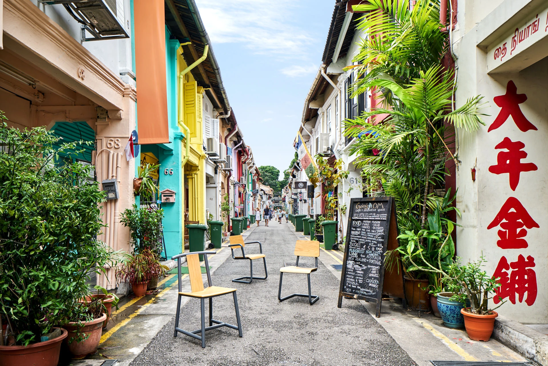 Three modern chairs with wooden seats and black metal frames displayed along a narrow colorful shophouse street with Chinese signage and potted plants.