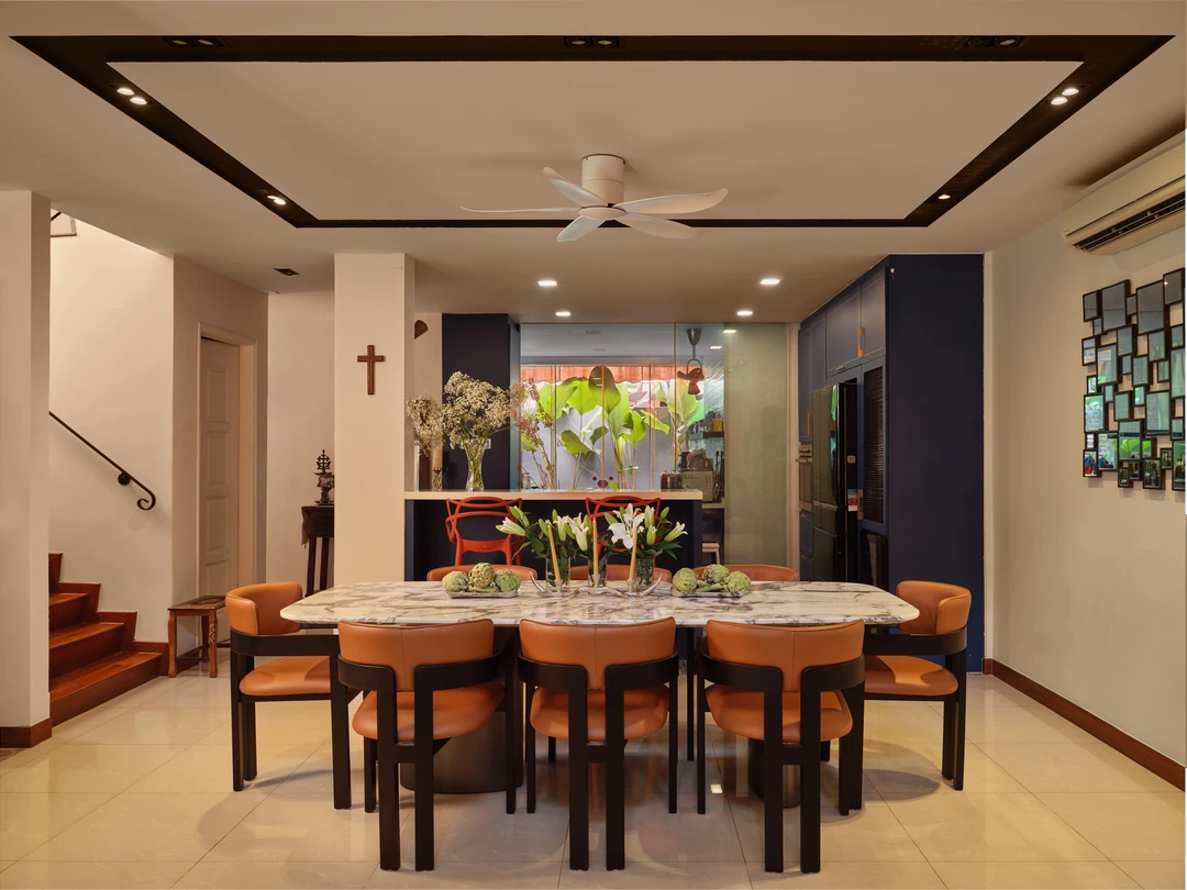 Serangoon Chuan Drive dining room by Nidhi Jain with marble dining table, orange chairs, staircase and leafy garden backdrop