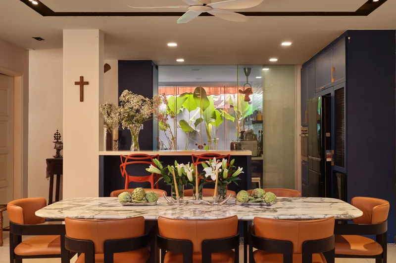Serangoon Chuan Drive dining room by Nidhi Jain with marble dining table, orange chairs, staircase and leafy garden backdrop