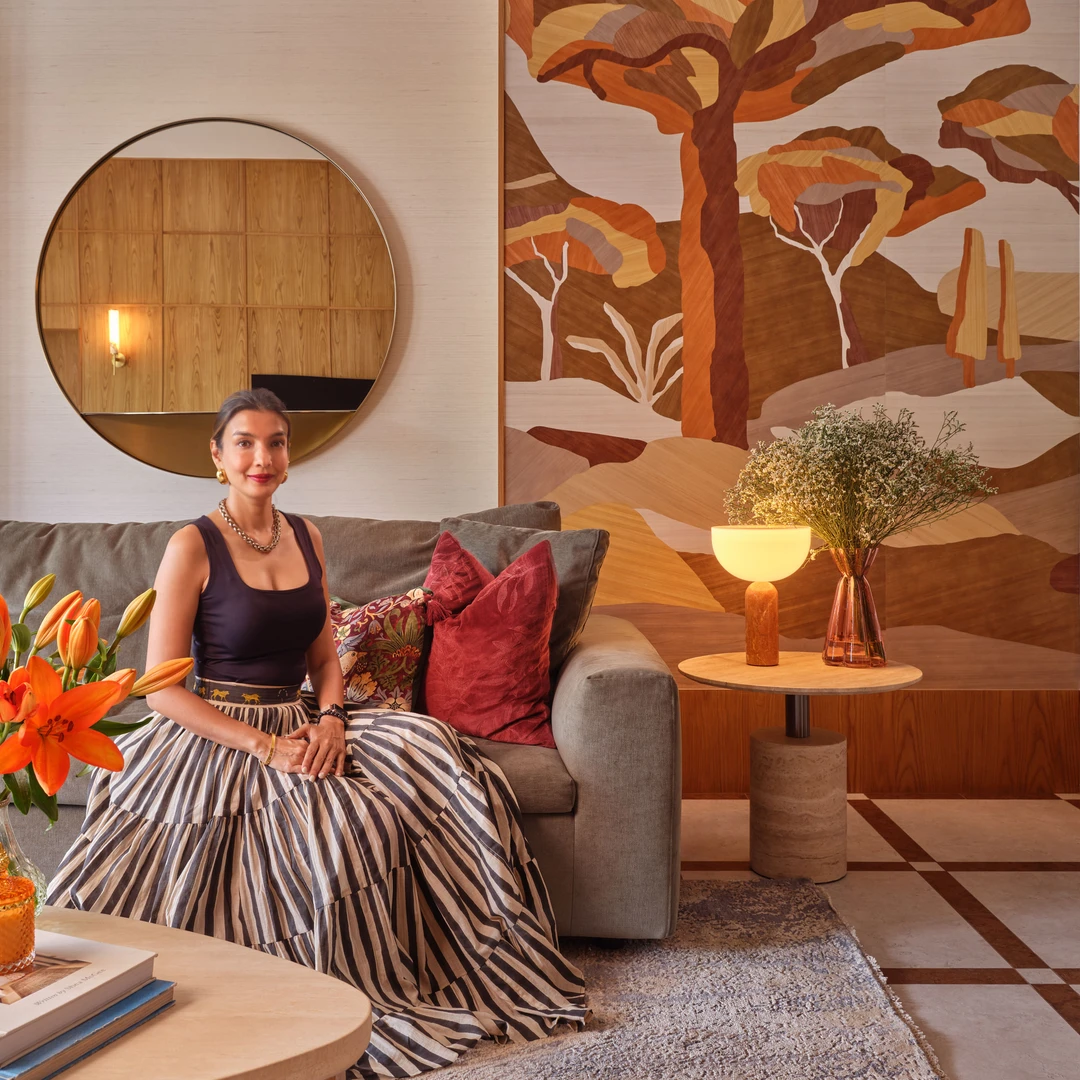 Interior designer Nidhi Jain seated in the Bayshore living room with botanical mural, round mirror and styled sofa