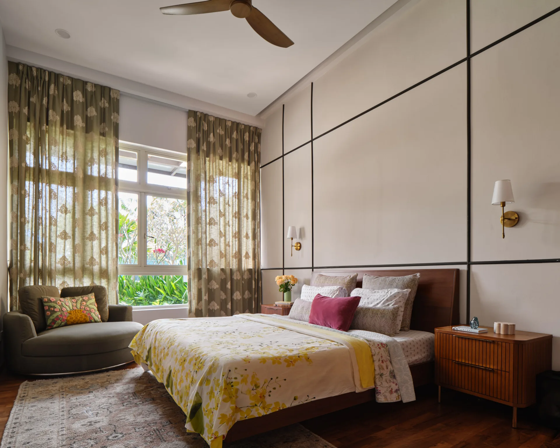 Bayshore bedroom by Nidhi Jain with paneled headboard wall, floral curtains, lounge chair and yellow botanical bedding, wide view
