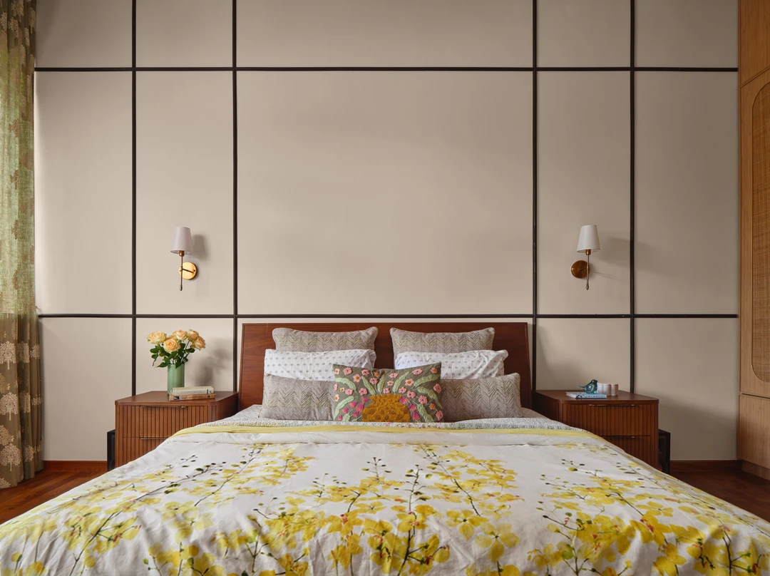 Bayshore bedroom bed styling by Nidhi Jain with wall sconces, floral bedding and tall paneled headboard wall, wide view