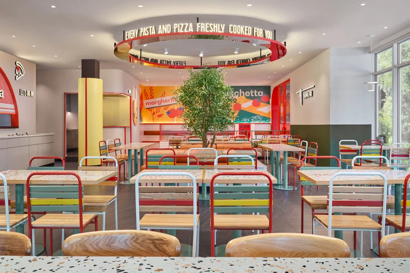 Full restaurant view with multicoloured seating, mural wall and central olive tree at PastaMania Sengkang