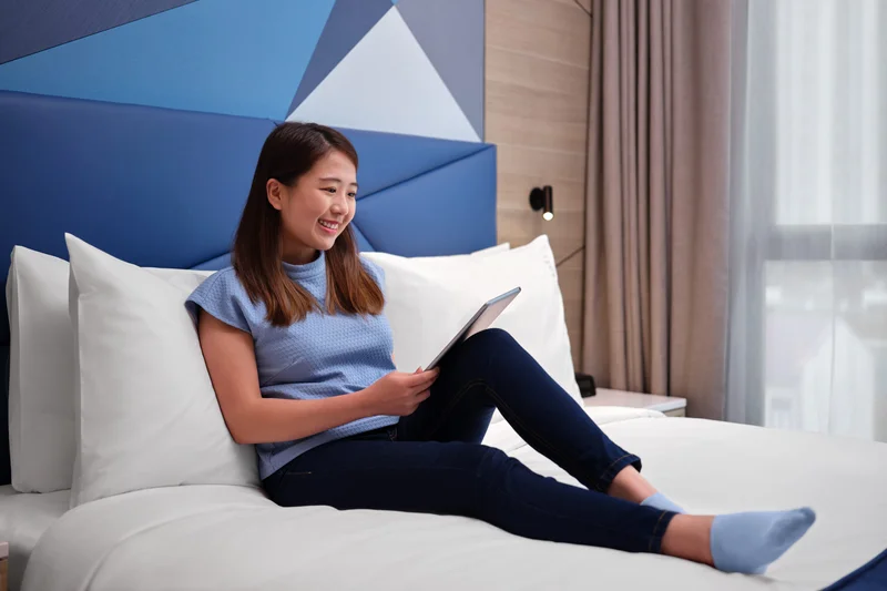 Woman with tablet on hotel bed against blue geometric headboard