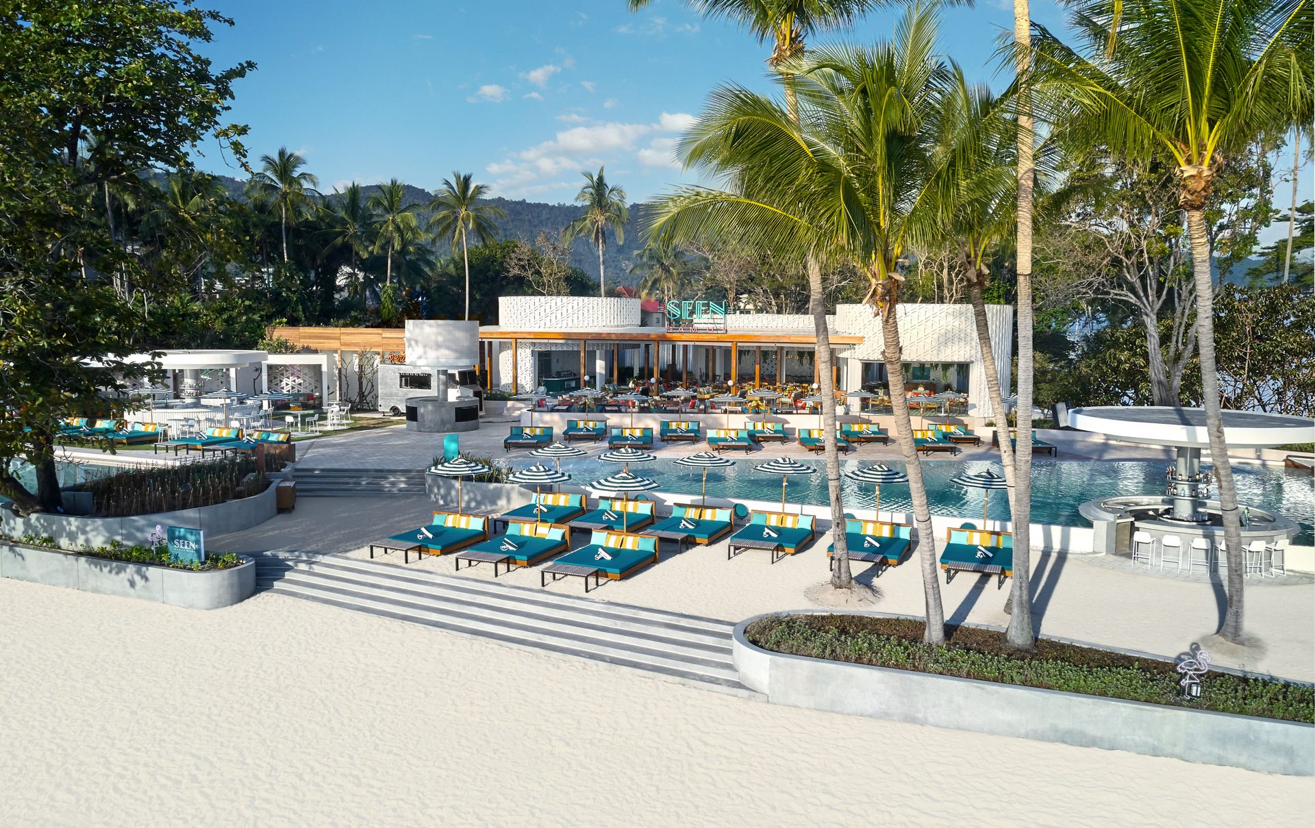 Tropical resort pool area with teal sun loungers, striped umbrellas and palm trees