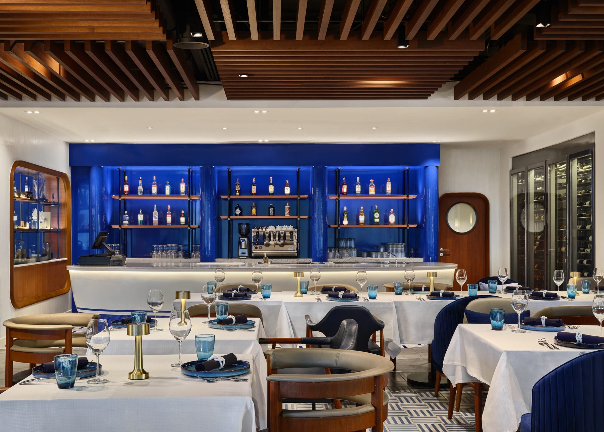 Nautical dining room with cobalt-blue backlit bar and slatted ceiling — Siam Yacht Club Bangkok restaurant photography