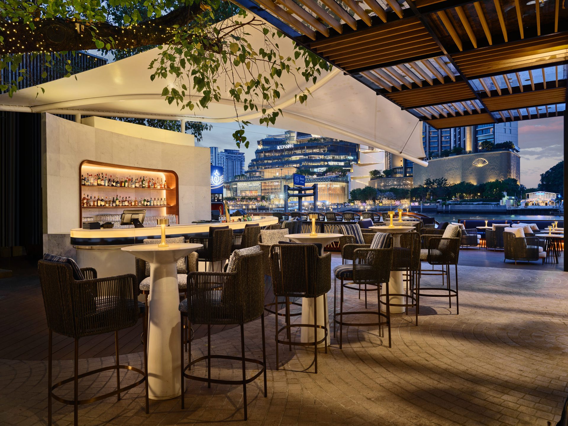 Twilight cocktail bar with rope stools and city skyline across river — Siam Yacht Club Bangkok hospitality photography