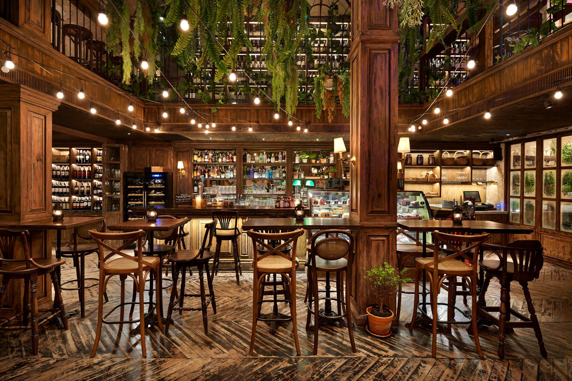 Central bar with wooden column, cross-back stools and mezzanine ferns above