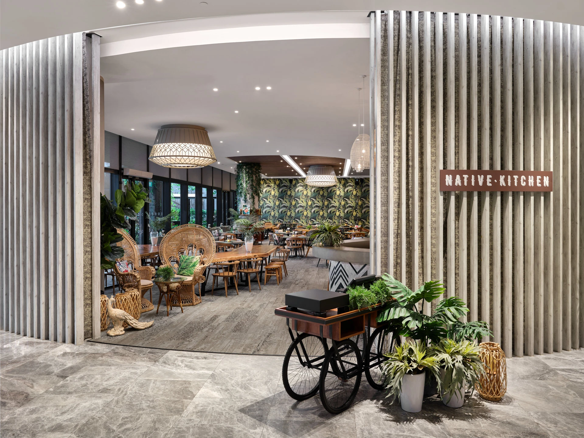 Restaurant entrance with curved timber facade, peacock chairs and vintage cart — Native Kitchen Village Hotel photography