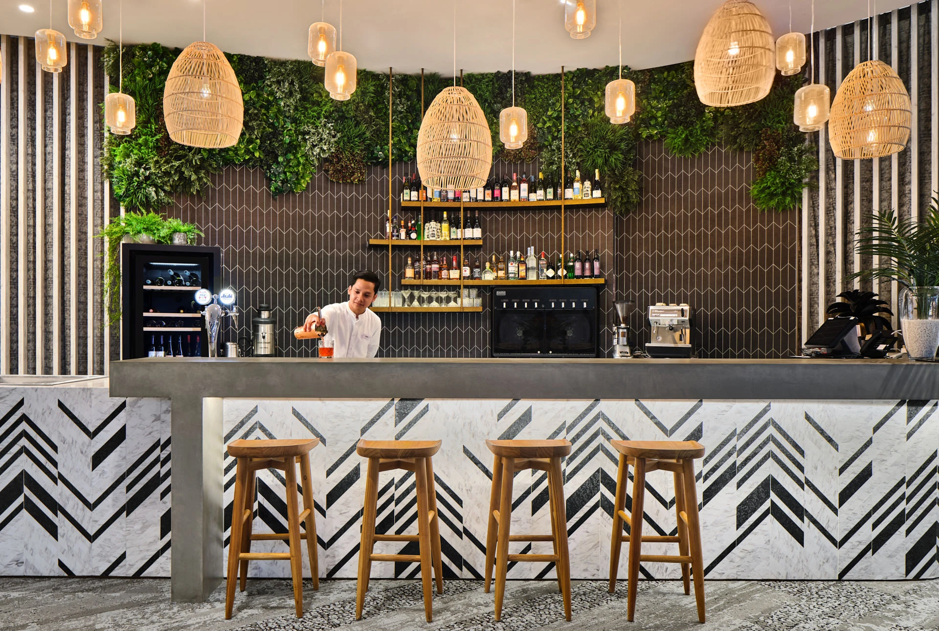 Cocktail bar with chevron marble front, bartender and rattan pendants — Village Hotel Sentosa hospitality photography