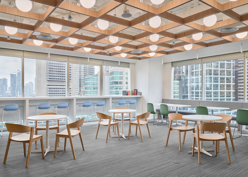 Ireland House Singapore break room with timber-grid ceiling, globe pendant lights, oak café tables and chairs, blue window-seat cushions and city skyline view