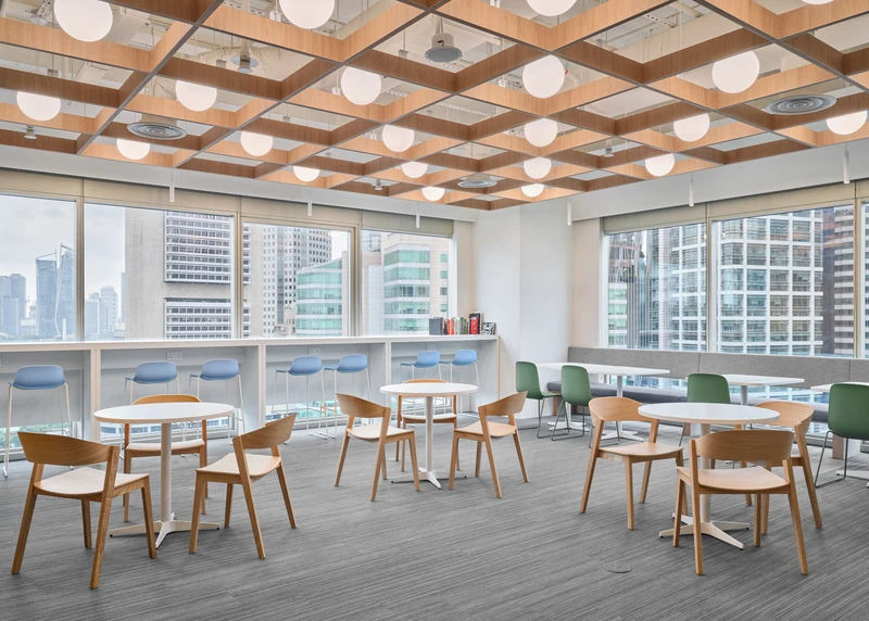 Ireland House Singapore break room with timber-grid ceiling, globe pendant lights, oak café tables and chairs, blue window-seat cushions and city skyline view