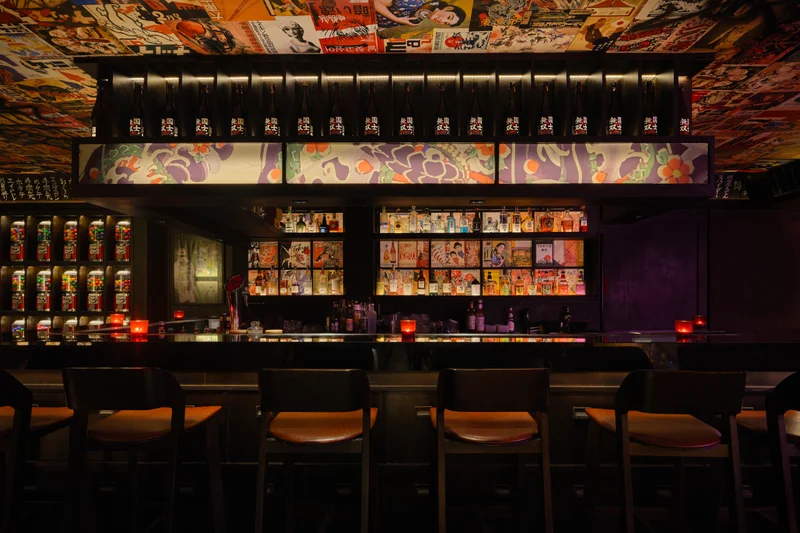 Yankii Robatayaki & Bar Bangkok bar counter with sake bottles, illuminated manga panels, and poster ceiling