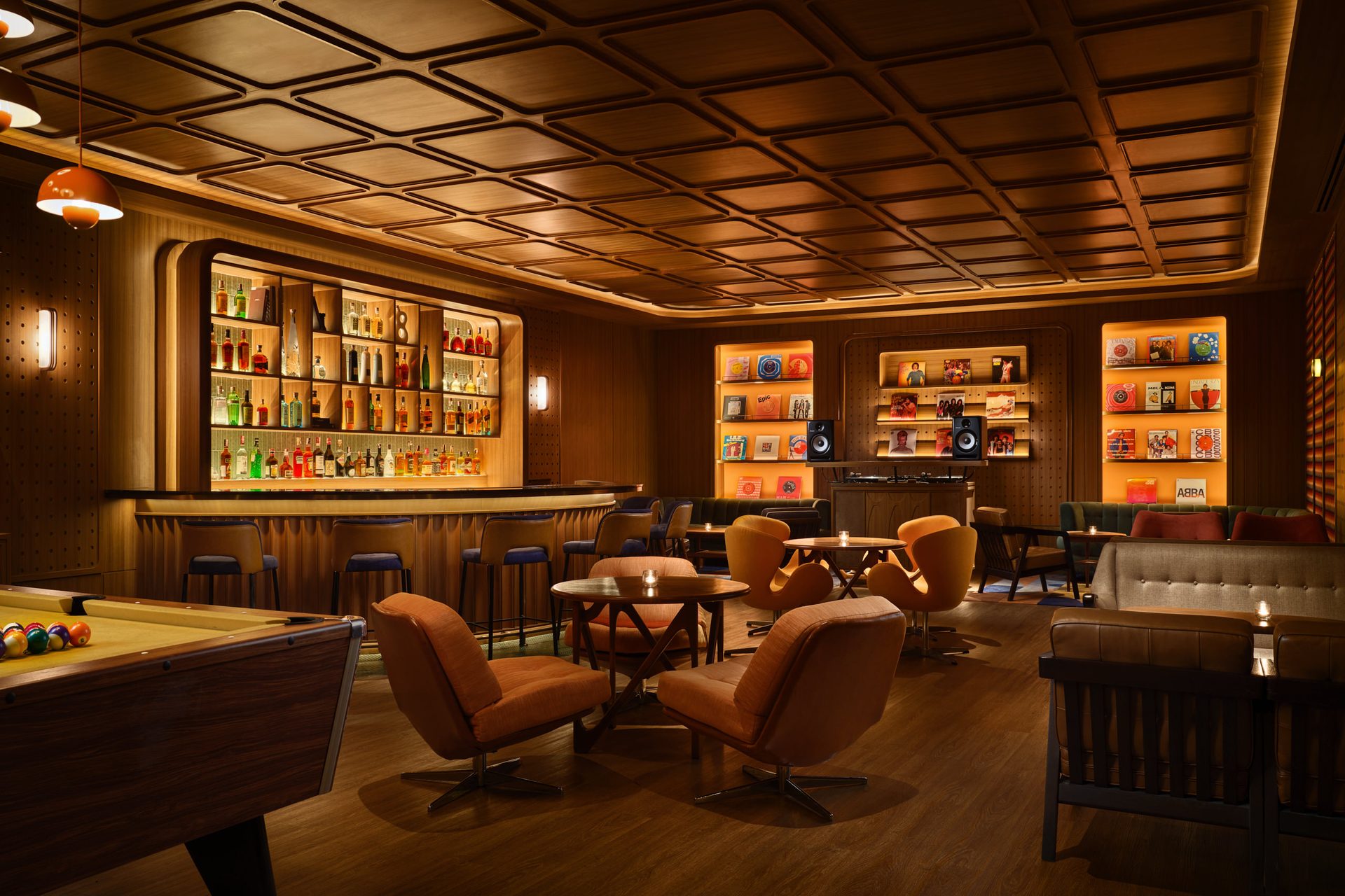 Retro lounge with wood paneling, backlit bar, pool table, swivel armchairs, and illuminated display shelves
